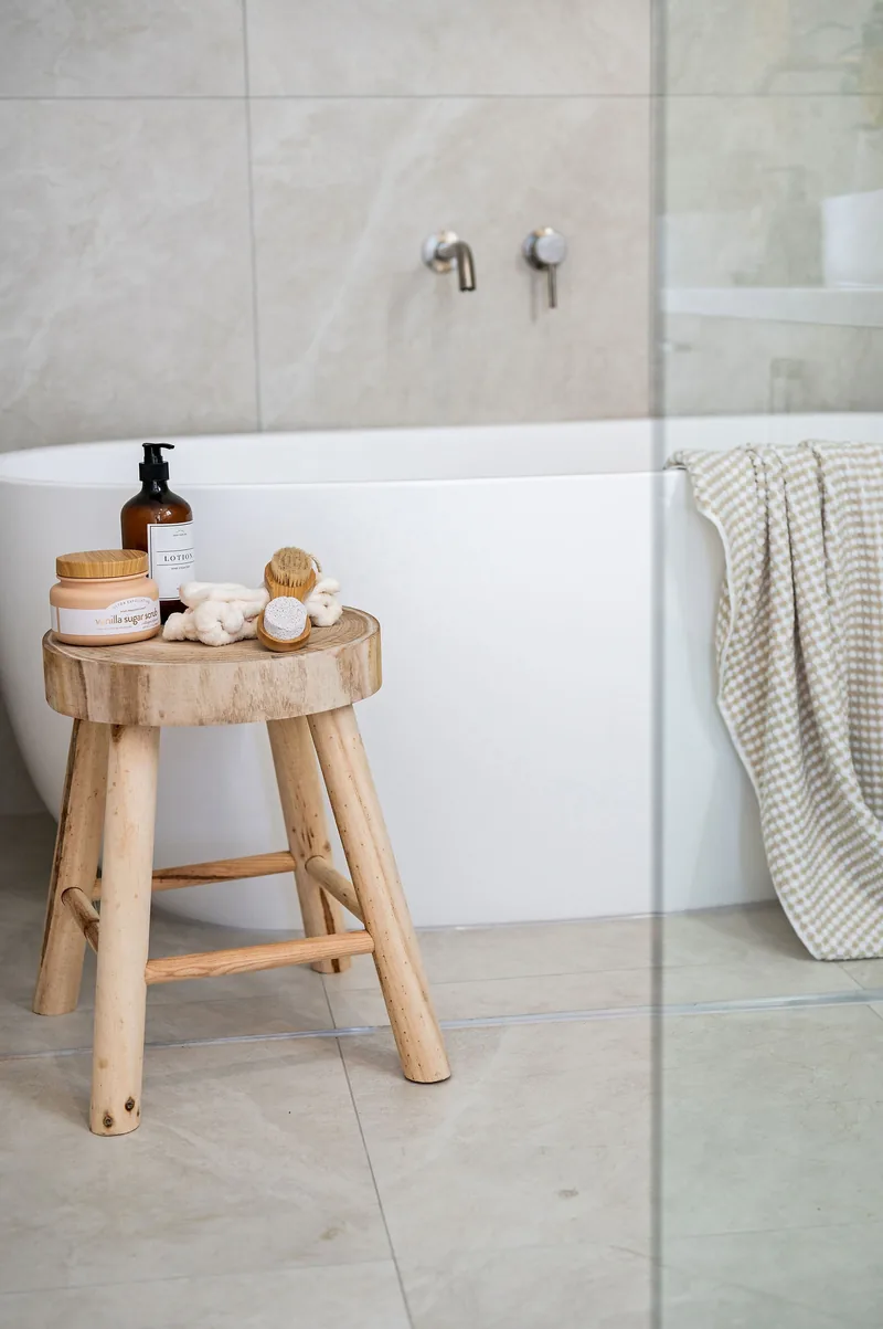 A bathroom styled with a timber stool, towels and amenities.