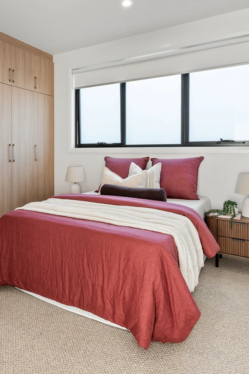 A master bedroom styled with deep red bedding and timber joinery.