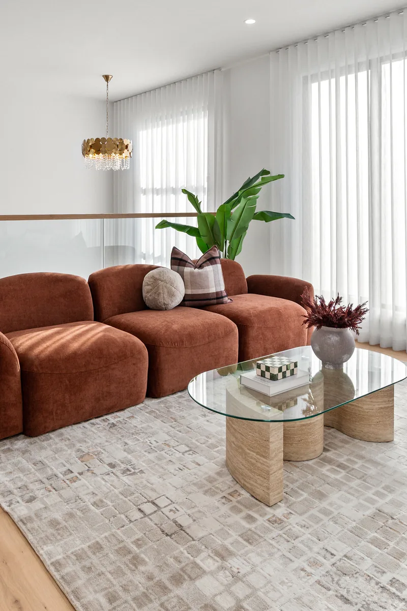 A styled living room with a rust modular sofa, glass coffee table and greenery.