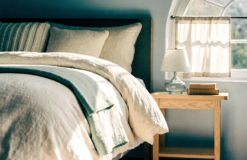 A styled bedroom with layered linen bedding and soft natural light.